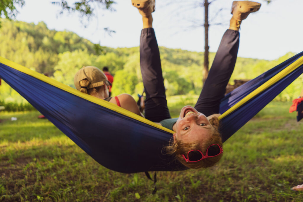 A girl is swinging around upside-down in a blue and yellow hammock. She is in a grassy area.